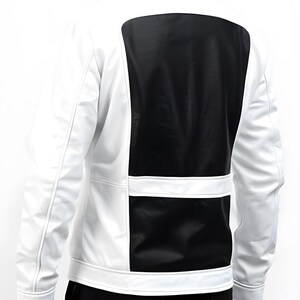 May include: White and black jacket with a modern design. The jacket features a white body with a large black panel on the back and a horizontal black panel on the lower back. The jacket has a stand-up collar and long sleeves.