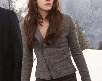 May include: A gray, textured jacket with a diagonal zipper and two small pockets. The jacket is paired with a dark gray skirt. The person in the image has long, brown hair and is standing in front of a snowy mountain backdrop.