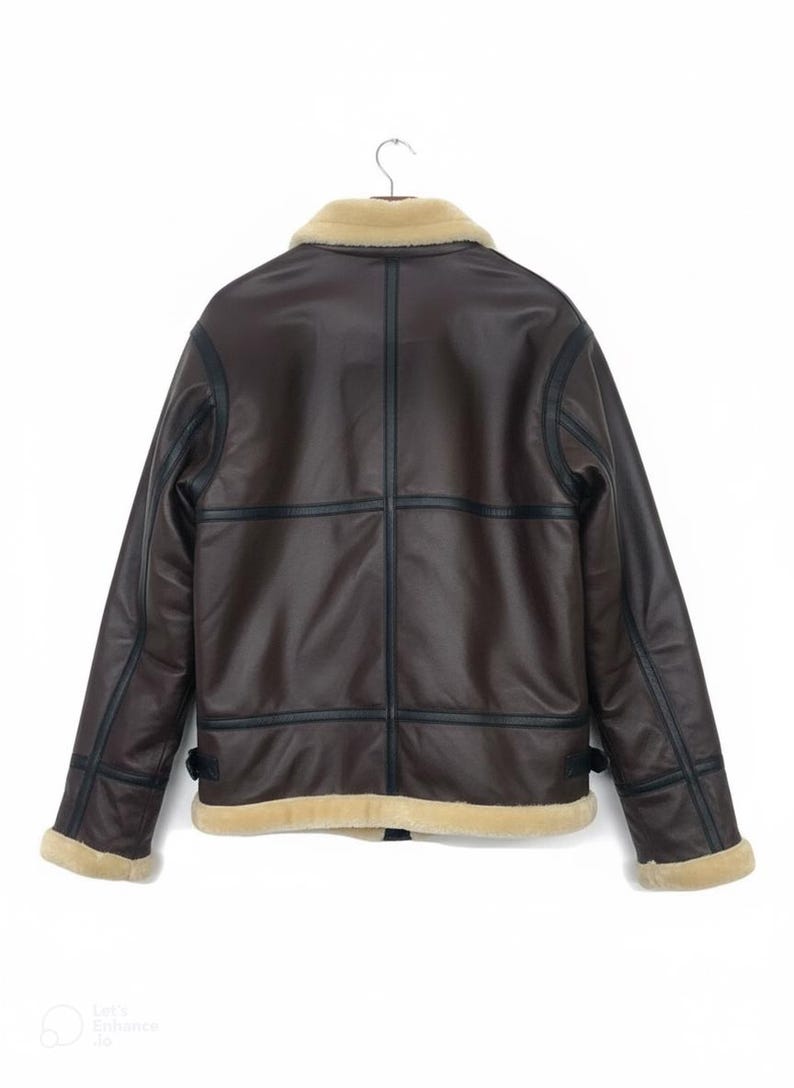 May include: Brown faux leather jacket with a cream-colored shearling collar and trim. The jacket features black trim and stitching details, with a classic aviator style. The back view shows the jacket hanging on a hanger.