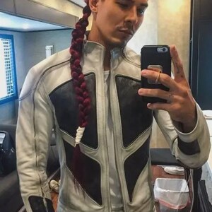 May include: A person wearing a white and black leather jacket and matching pants. The jacket has a unique design with black panels and a zipper closure. The person has red hair styled in a braid. They are holding a black smartphone.