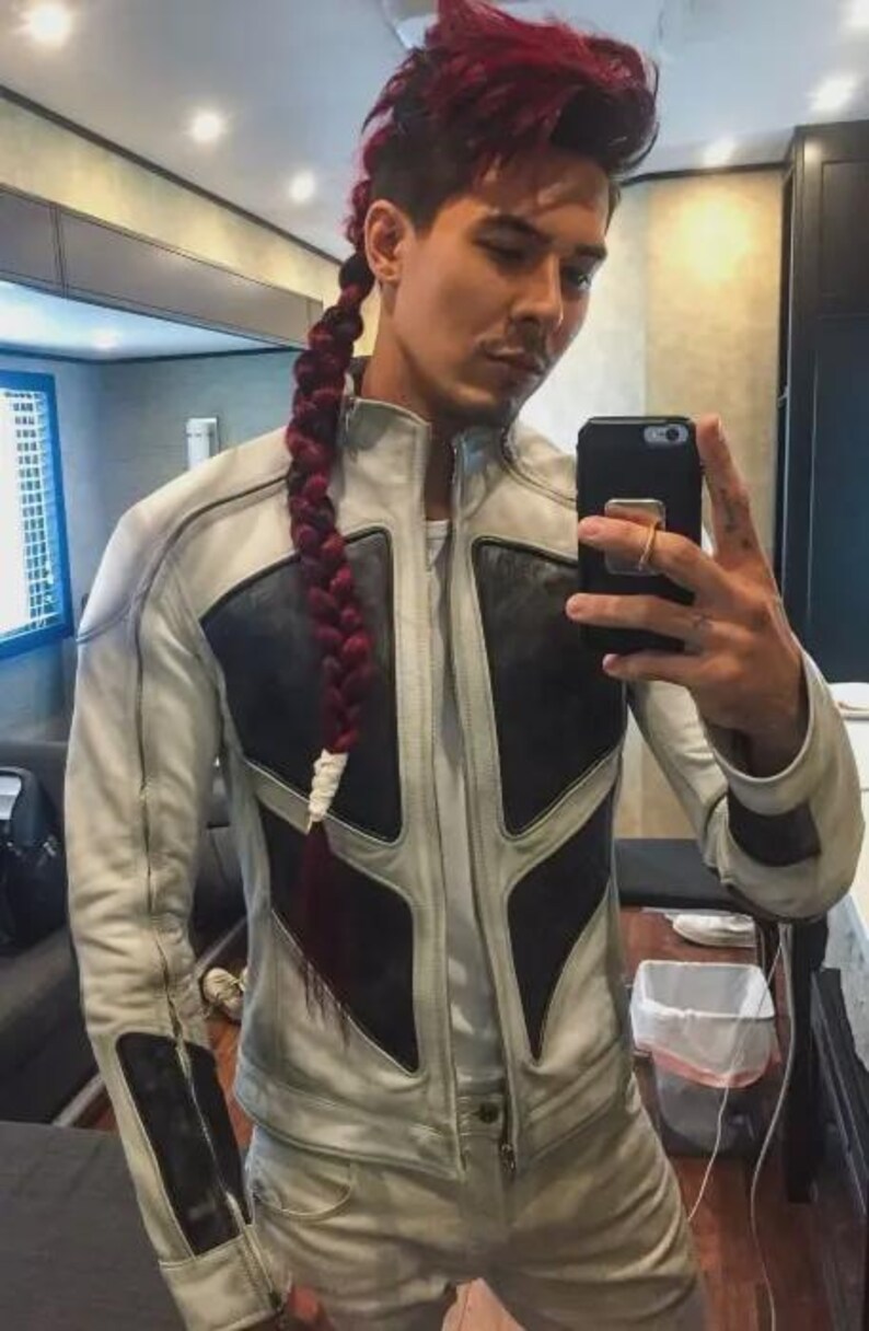 May include: A person wearing a white and black leather jacket and matching pants. The jacket has a unique design with black panels and a zipper closure. The person has red hair styled in a braid. They are holding a black smartphone.
