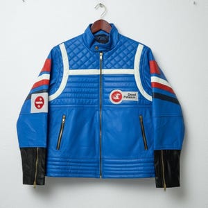 May include: A blue leather jacket with a quilted design on the shoulders and upper chest. The jacket features white stripes, red and blue accents on the sleeves, and a "Dead Pekasus" patch. Black cuffs with zippers complete the design.