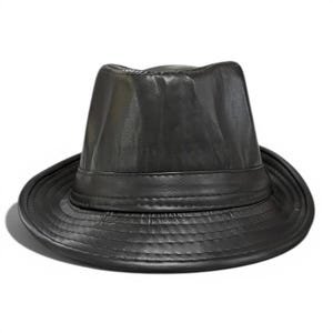 Op de afbeelding: Een zwarte fedora hoed gemaakt van een glad, licht reflecterend materiaal. De hoed heeft een ingedeukte kroon, een gestructureerde rand met zichtbare horizontale stiksels en een bijpassende zwarte band rond de basis van de kroon.