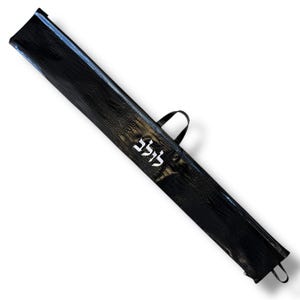 Puede incluir: Funda de transporte negra texturizada con asa y cremallera plateada. La funda tiene un patrón similar al de un reptil y la palabra "לולב" en blanco. La funda está diseñada para guardar un objeto largo y delgado.