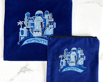 May include: Two navy blue velvet pouches. Each pouch features an embroidered design of a city with domes and arches in shades of blue, with text in Hebrew. One pouch is larger than the other.