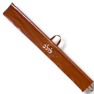 Puede incluir: Una funda de cuero marrón con asa y lazo en el extremo. La funda tiene una superficie texturizada y texto hebreo blanco. La funda está diseñada para guardar un objeto largo y delgado.