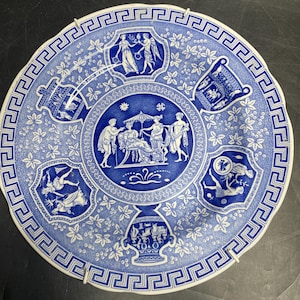 May include: A blue and white decorative plate with a Greek key border. The plate features detailed illustrations of classical figures and scenes within decorative panels. The overall design includes floral and geometric patterns.