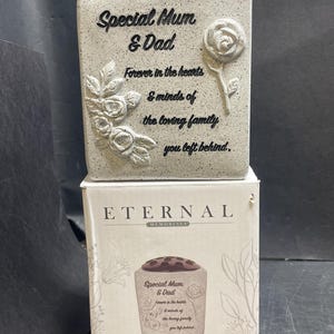 May include: A light grey memorial flower pot with the text "Special Mum & Dad" and floral detailing. The pot has a black top and sits on a box that reads "Eternal Memorials".