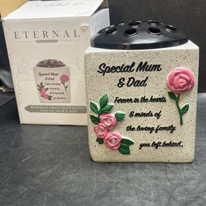May include: A memorial grave flower pot with the text "Special Mum & Dad" and a floral design. The pot is off-white with a black top and includes the words "Forever in the hearts & minds of the loving family you left behind."