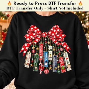Peut inclure: Un sweat-shirt noir avec un grand nœud rouge à pois blancs. Suspendus au nœud se trouvent des illustrations de cassettes VHS de films de Noël, notamment Rudolph, A Charlie Brown Christmas, The Santa Clause, Frosty, Elf, Christmas Vacation, How the Grinch Stole Christmas et Home Alone.