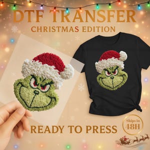 Pode incluir: Uma camiseta preta e uma transferência DTF com um personagem verde com um chapéu de Papai Noel vermelho e branco. A transferência está pronta para prensar e faz parte da edição de Natal.