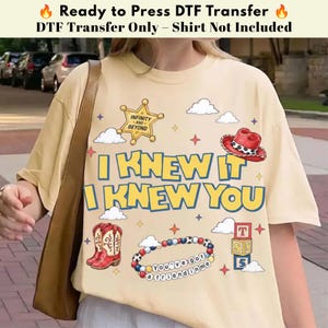 以下が含まれることがあります： クリーム色のTシャツ。I KNEW IT I KNEW YOUの文字、INFINITY AND BEYONDと書かれた金色の保安官バッジ、赤いカウボーイハット、赤いカウボーイブーツ、YOU'VE GOT A FRIEND IN MEと書かれたビーズブレスレット、積み木のグラフィックがプリントされています。