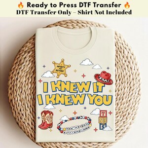 以下が含まれることがあります： クリーム色のDTF転写シート。青と黄色の文字で「I KNEW IT I KNEW YOU」と書かれています。グラフィックには「INFINITY AND BEYOND」と書かれた金色の保安官バッジ、赤いカウボーイハット、赤いカウボーイブーツ、カラフルなビーズのブレスレット、アルファベットの積み木が含まれています。