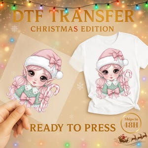 Peut inclure: Design DTF TRANSFER Édition de Noël avec une jolie fille elfe aux cheveux roses, un chapeau rose et un sucre d'orge. Le motif est prêt à être pressé sur un t-shirt blanc. Le texte "READY TO PRESS" est visible.