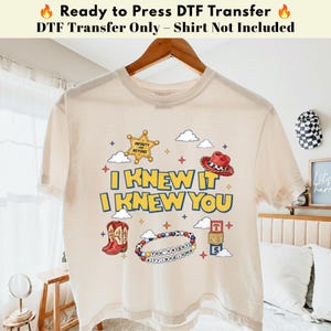 以下が含まれることがあります： クリーム色のTシャツ。I KNEW IT I KNEW YOUの文字、INFINITY AND BEYONDと書かれた保安官バッジ、赤いカウボーイハット、赤いカウボーイブーツ、ビーズのブレスレット、T S Sの文字が書かれた積み木が描かれたグラフィックプリントが施されています。