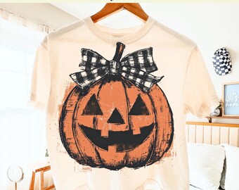 May include: A cream-coloured t-shirt with a distressed orange jack-o'-lantern design and a black and white plaid bow. The text at the top reads "Ready to Press DTF Transfer" and "DTF Transfer Only - Shirt Not Included".