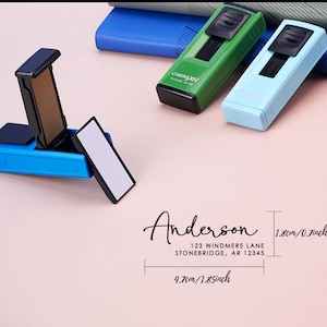 May include: A blue address stamp with a black ink pad is open, next to green and light blue stamps. The text "Anderson" and an address are displayed. The stamps are 1.8cm x 4.7cm (0.7in x 1.85in).