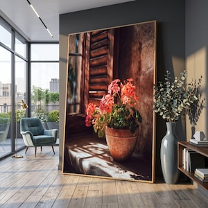 Pode incluir: Uma impressão de arte emoldurada com um vaso de terracota com vibrantes flores rosa numa janela ensolarada. A imagem captura uma cena rústica com persianas de madeira e uma parede de pedra, criando uma atmosfera acolhedora. A obra de arte é exibida num interior moderno.