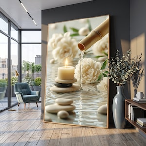 May include: A framed print shows a tranquil spa scene. A lit candle rests on stacked stones, with water flowing from a bamboo spout. White flowers and smooth stones are in the water, creating a calming aesthetic.