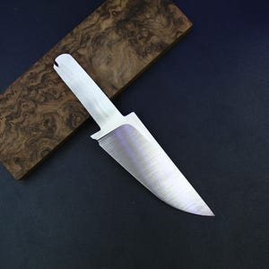 May include: A stainless steel knife blade with a wooden handle. The blade is angled, with a sharp point. The wooden handle is a light brown color with a unique wood grain pattern. The background is a dark blue.