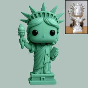 May include: A mint green vinyl figure of the Statue of Liberty, holding a torch and a tablet. The figure has large black eyes and is mounted on a rectangular base. A smaller, silver version is in the upper right corner.