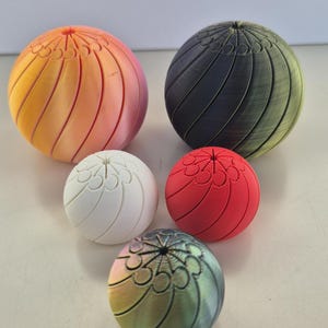 May include: Five spherical decorative objects in various colours. The objects have a ribbed design with a floral pattern on top. Colours include orange to pink, black to green, white, red, and iridescent.