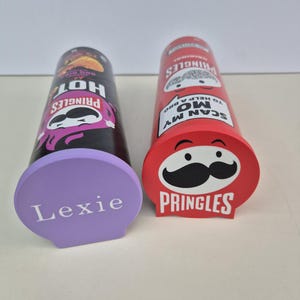 May include: Two Pringles chip containers, one black and one red, with custom-made bases. The black container is labeled "Hot" and the red one has the Pringles logo. A purple base is labeled "Lexie".