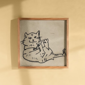 May include: A framed artwork with a playful black and white cat illustration. The cat is drawn lying on its back, paws raised. The artwork is set against a neutral backdrop and framed in light-coloured wood.