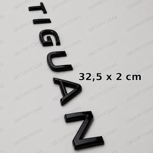 May include: A set of individual black, glossy, three-dimensional letters spelling the word TIGUAZ arranged vertically. The letters have a clean, modern font style. The text 32,5 x 2 cm is printed in black next to the letters, indicating the dimensions.