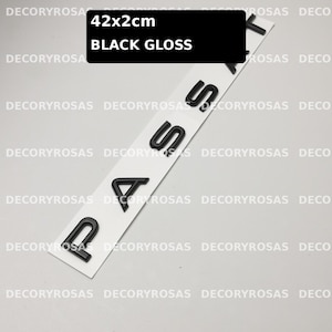May include: A set of black gloss letters spelling PASSAT arranged vertically on a white adhesive strip. The text on the black label indicates dimensions of 42x2cm and the finish as black gloss. The letters are individual, raised, and glossy.