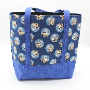 May include: A blue tote bag with a repeating pattern of a character from a popular science fiction series. The bag has blue handles and a blue base. The interior of the bag is black.