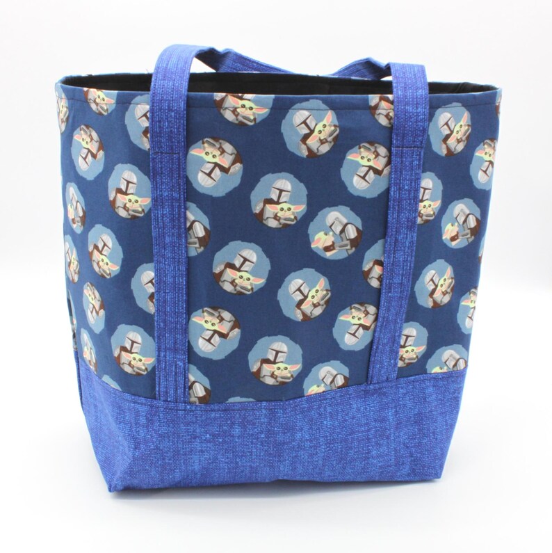 May include: A blue tote bag with a repeating pattern of a character from a popular science fiction series. The bag has blue handles and a blue base. The interior of the bag is black.