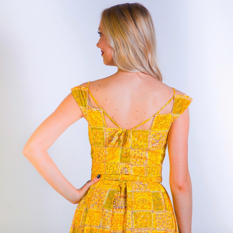 May include: A yellow and green patterned dress with a low back and a tie detail at the back of the neck.