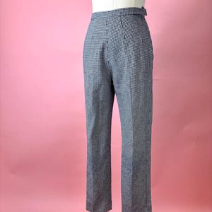 May include: High-waisted, black and white checkered pants. The pants are displayed on a mannequin against a pink background. The pants have a straight leg cut and a button closure.