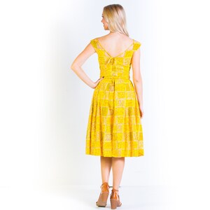 May include: A yellow midi dress with a checkered pattern and a tie at the back. The dress has a fitted bodice and a full skirt.