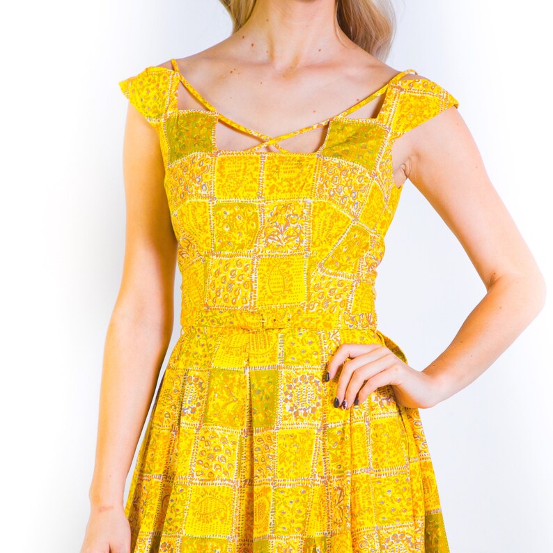 May include: A yellow dress with a patchwork design and a criss-cross neckline.