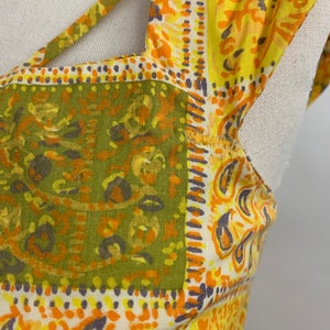 May include: Close-up of a yellow, orange, and green patterned fabric with a paisley design. The fabric has a cut-out detail at the neckline.