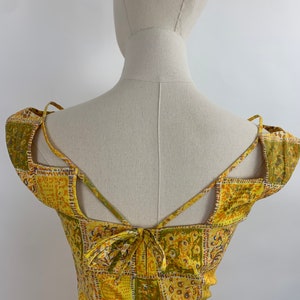 May include: Yellow and green patterned dress with a criss-cross back and a tie at the back.