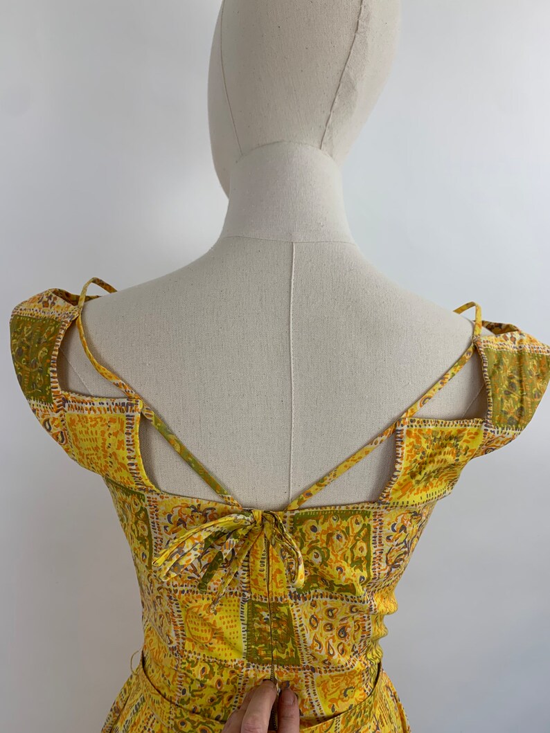 May include: Yellow and green patterned dress with a criss-cross back and a tie at the back.