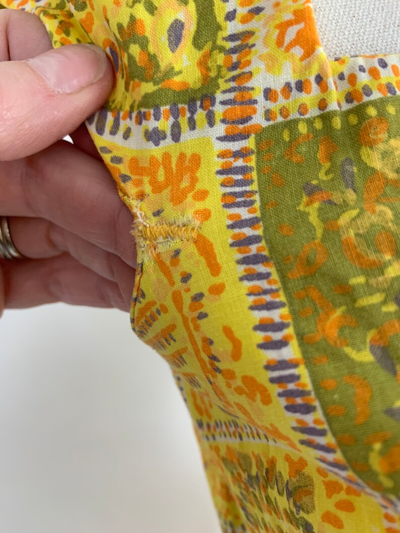 May include: Close-up of a yellow fabric with a geometric pattern in shades of orange, green, and purple. The fabric has a slightly distressed look, with some fraying along the edges.