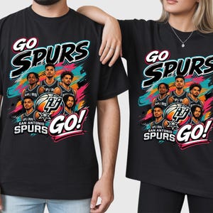 May include: Black t-shirts with a colorful graphic featuring the text "GO SPURS" and a basketball team illustration. The design includes the words "SAN ANTONIO SPURS" and "GO!" in a dynamic layout.
