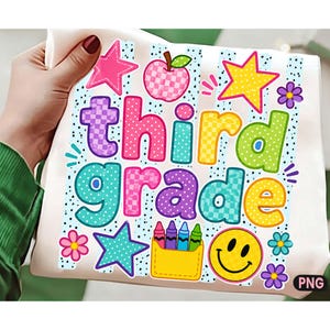 May include: A white fabric surface featuring a colorful graphic with the text "third grade" in bubble letters. The design includes a checkered apple, stars, flowers, a smiley face, and a yellow pocket containing five crayons on a dotted background.