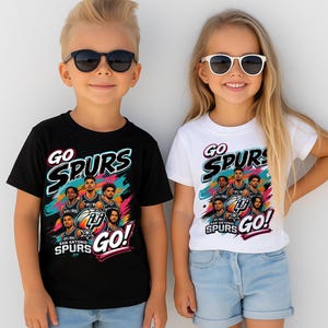 May include: Two children wearing black and white t-shirts with a colorful graphic design. The shirts feature the text "GO SPURS GO!" and an image of the San Antonio Spurs basketball team.