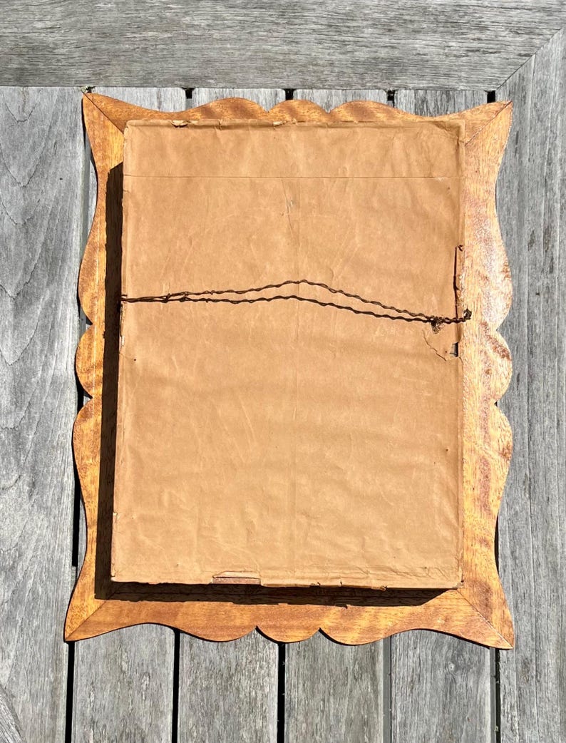 May include: Back of a framed artwork with a scalloped wooden frame. The frame is a light brown color. The artwork is covered with brown paper and secured with wire.