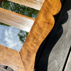 May include: A wooden framed mirror with a scalloped edge. The frame is a warm brown color with visible wood grain. The mirror reflects a view of the sky and trees. The mirror is rectangular.