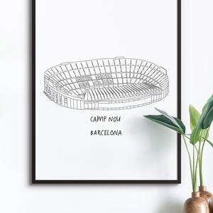 May include: Black framed print featuring a line drawing of Camp Nou stadium in Barcelona. The stadium's name and city are printed below the image. The words "Mes Que Un Club" are visible on the stadium.