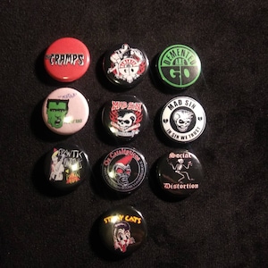 May include: A collection of ten round pinback buttons with various designs and text. The buttons feature images and text such as "CRAMPS", a green Frankenstein, and "Social Distortion". The buttons are in various colors, including red, black, and white.