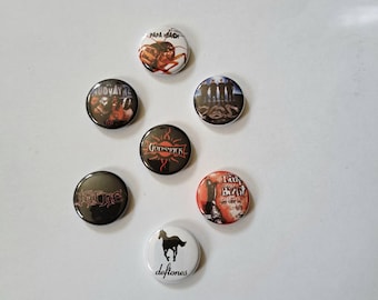 May include: A collection of seven round pinback buttons featuring band logos and artwork. The buttons display various designs, including band names like "Deftones" and "Godsmack," and images such as a horse silhouette and a cockroach.