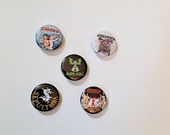 May include: A collection of five round metal pinback buttons featuring band logos and artwork. The buttons display the logos of Exodus, Testament, Overkill, Sepultura, and Kreator. The buttons are in various colors, including black, white, red, and green.