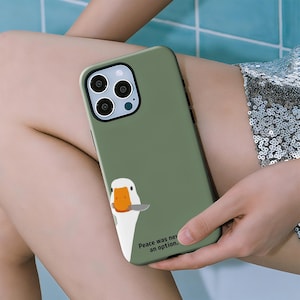 May include: Olive green phone case featuring a cartoon goose with a knife. The goose has a white body, orange beak, and is holding a silver knife. The text "Peace was never an option." is printed on the case.